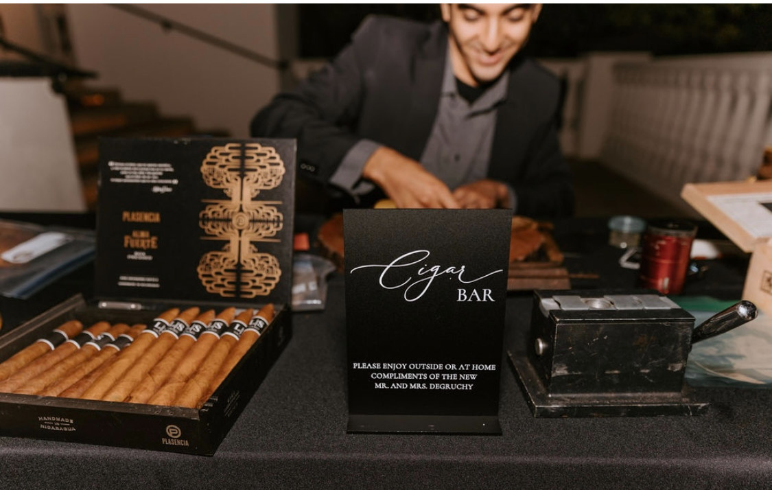 Elegant black cigar bar sign beside an open box of cigars